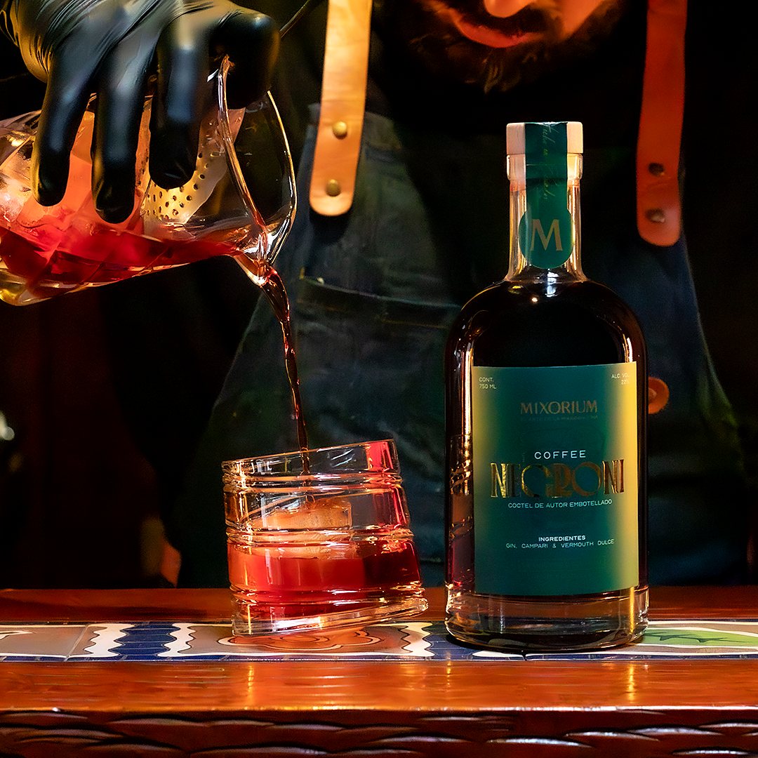 Un bartender sirve el cóctel desde un vaso mezclador, junto a la botella