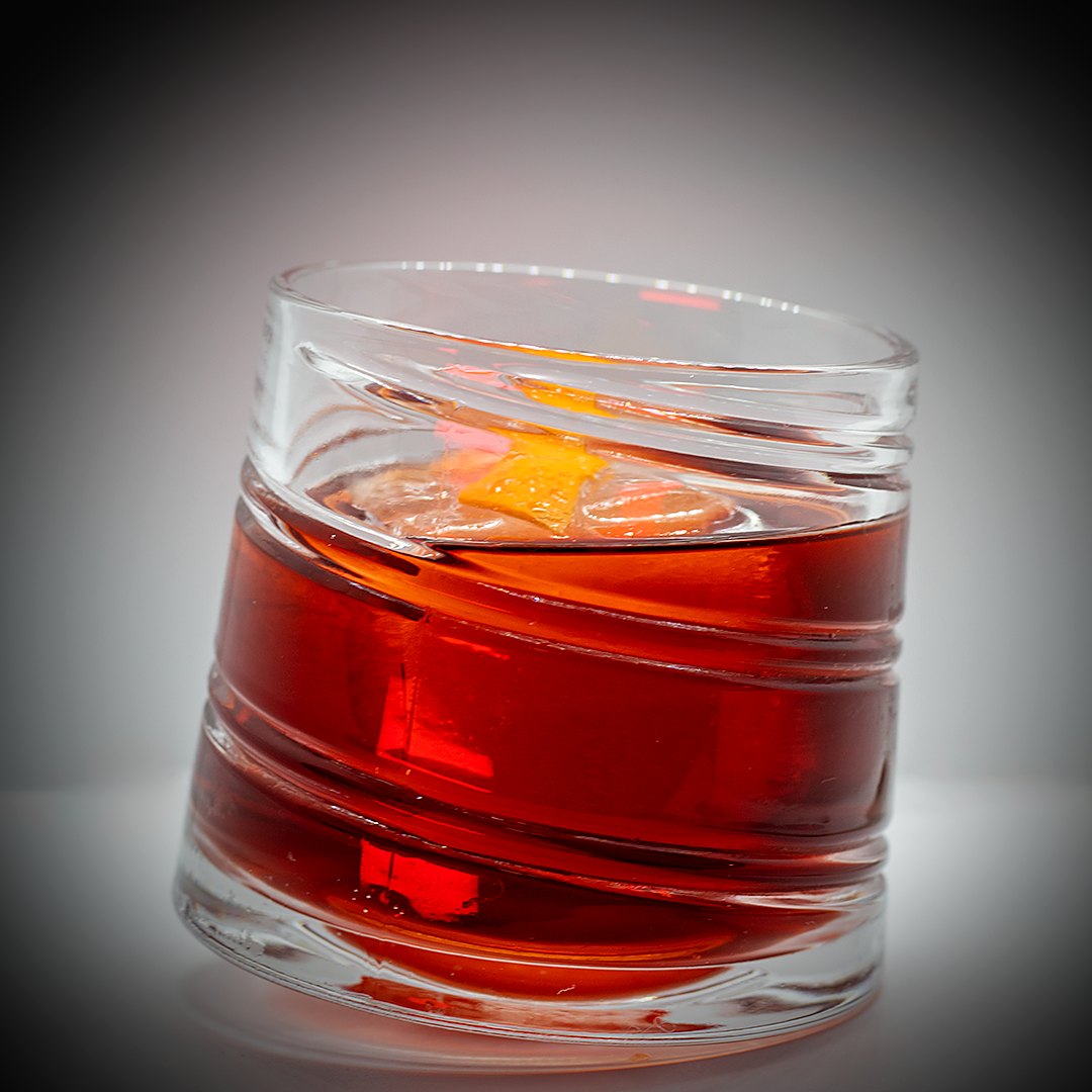 Primer plano del Coffee Negroni en un vaso inclinado, con hielo y piel de naranja